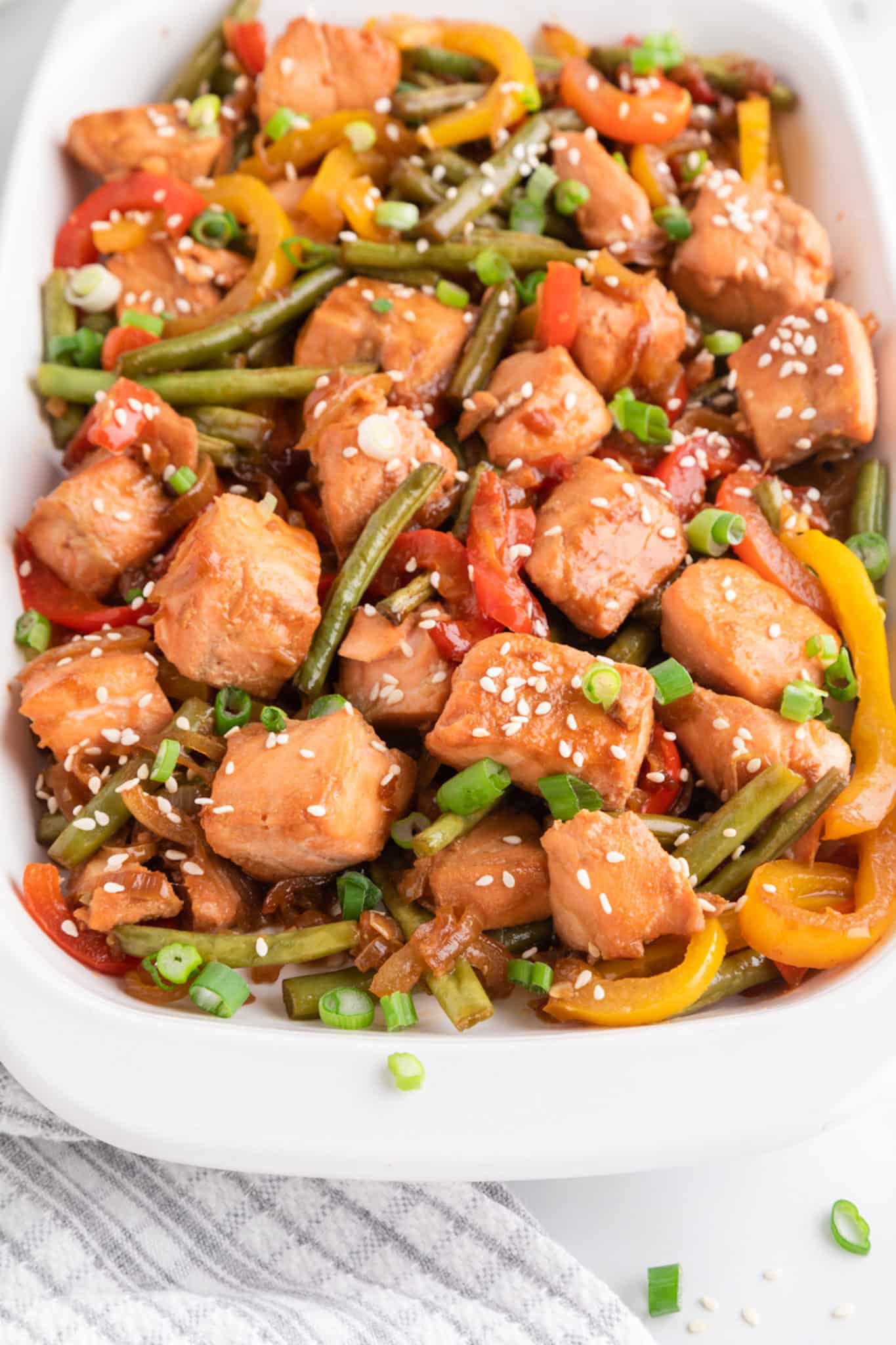 Close up of salmon veggie stir fry in a white serving dish.