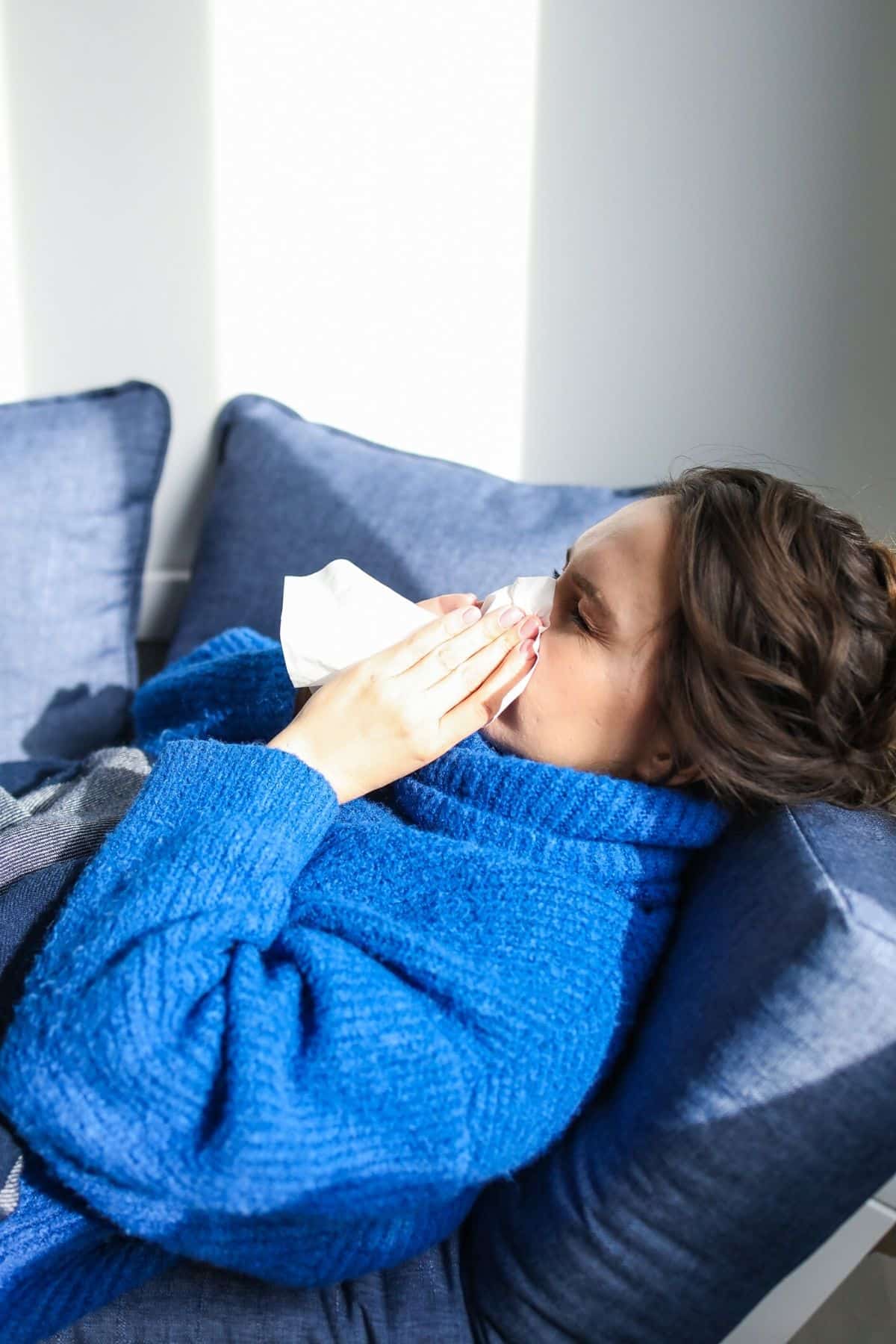 woman in blue sweater blowing nose.