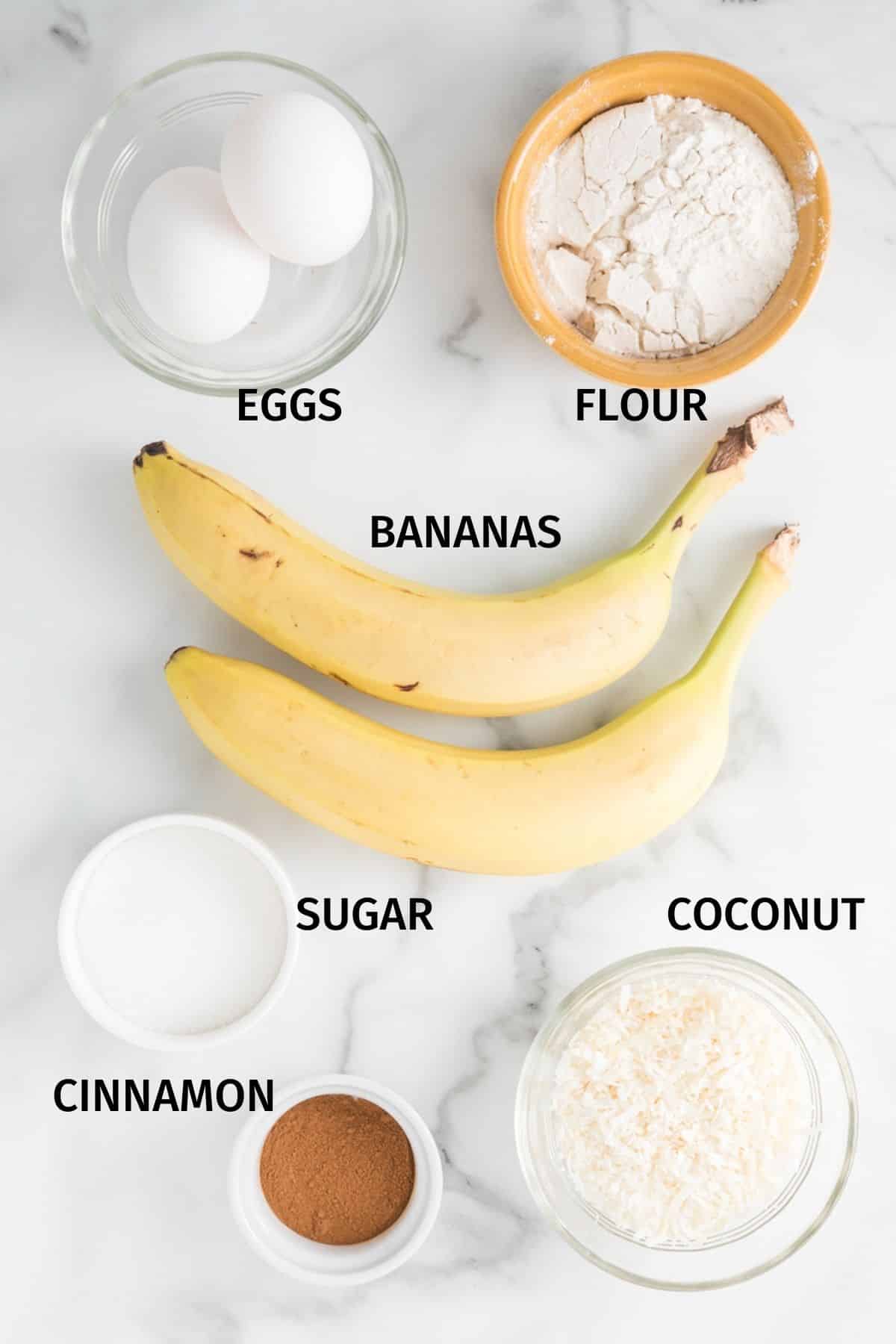 Ingredients for coconut banana fritters in small bowls on a white surface.