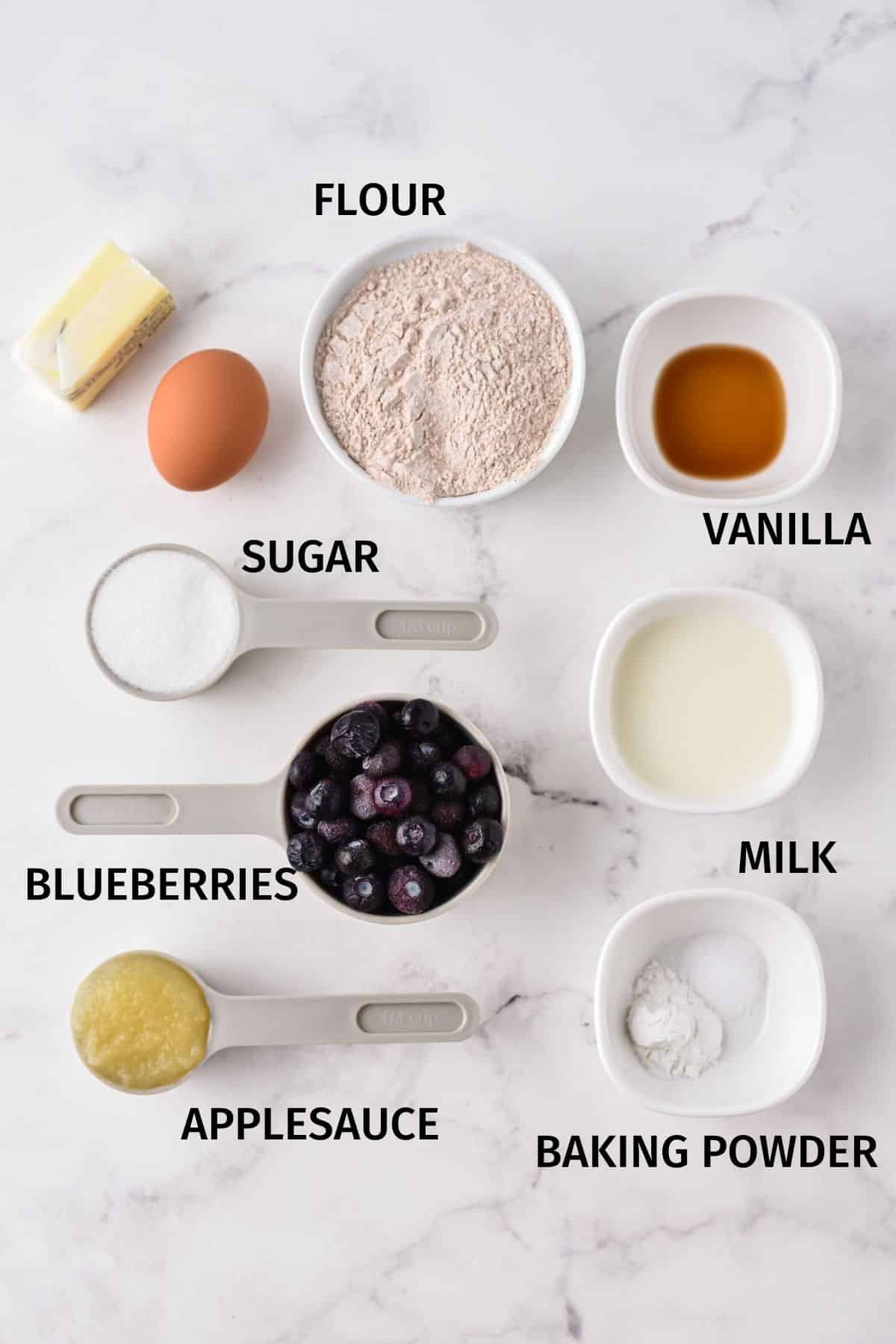 Measured ingredients for blueberry muffins in bowls on a white surface.