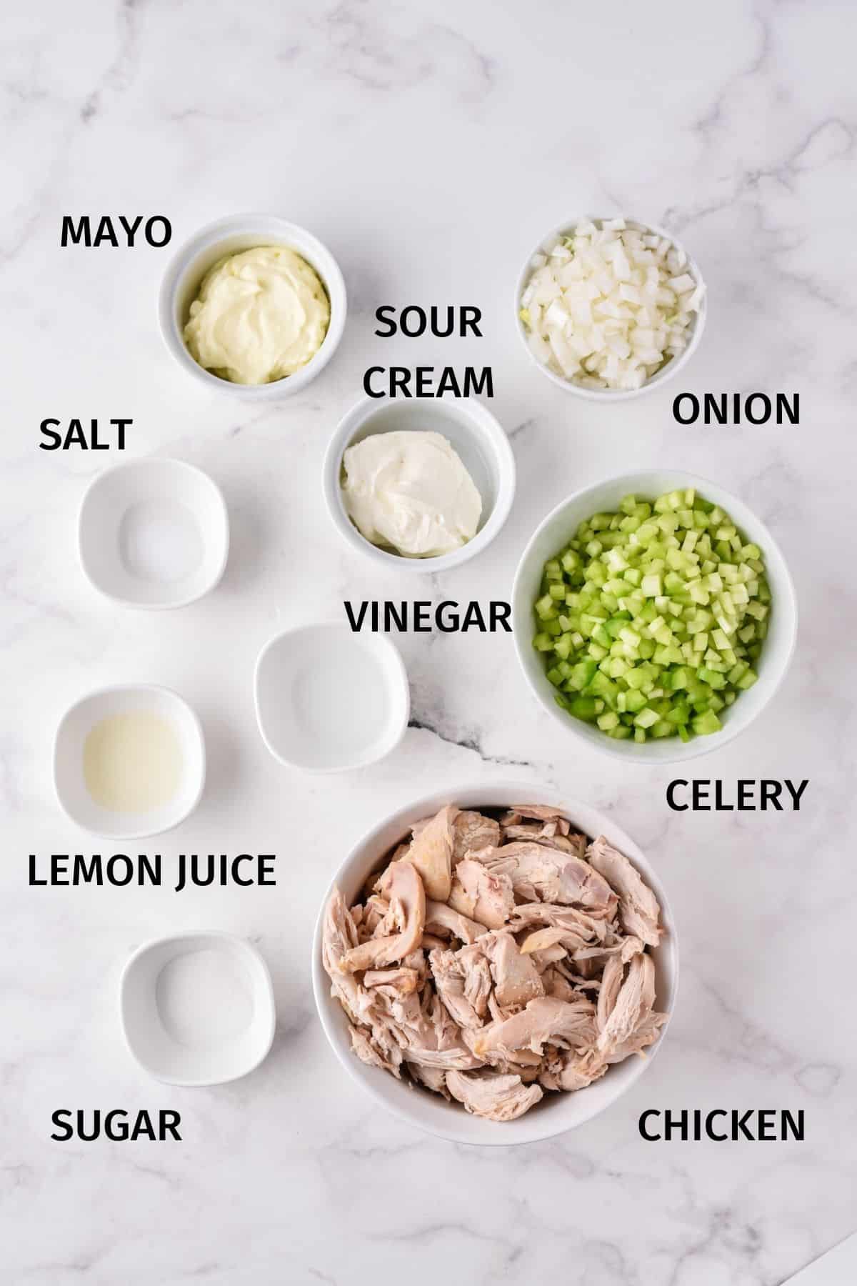 Ingredients to make chicken salad in small bowls on a white surface.