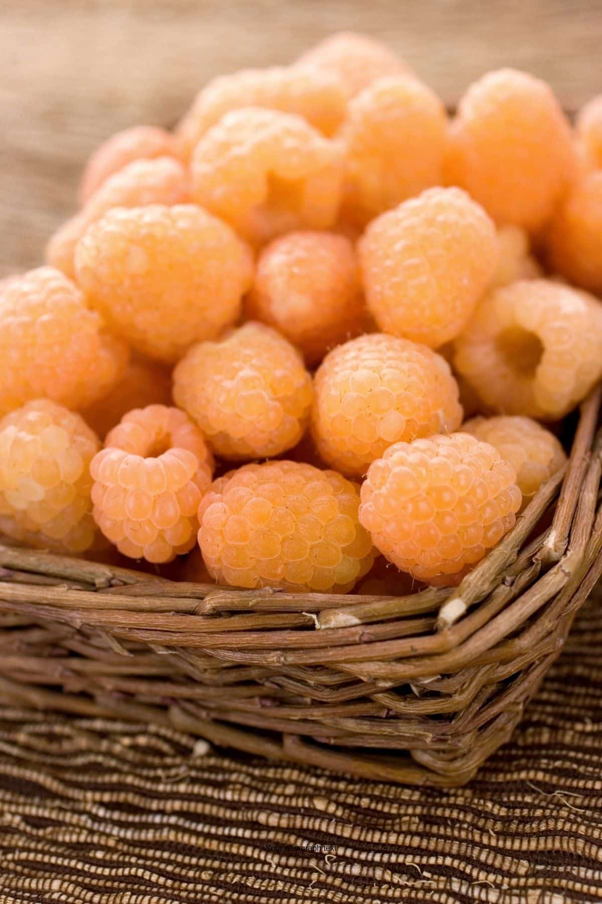 Golden raspberries in a woven basket on a table.