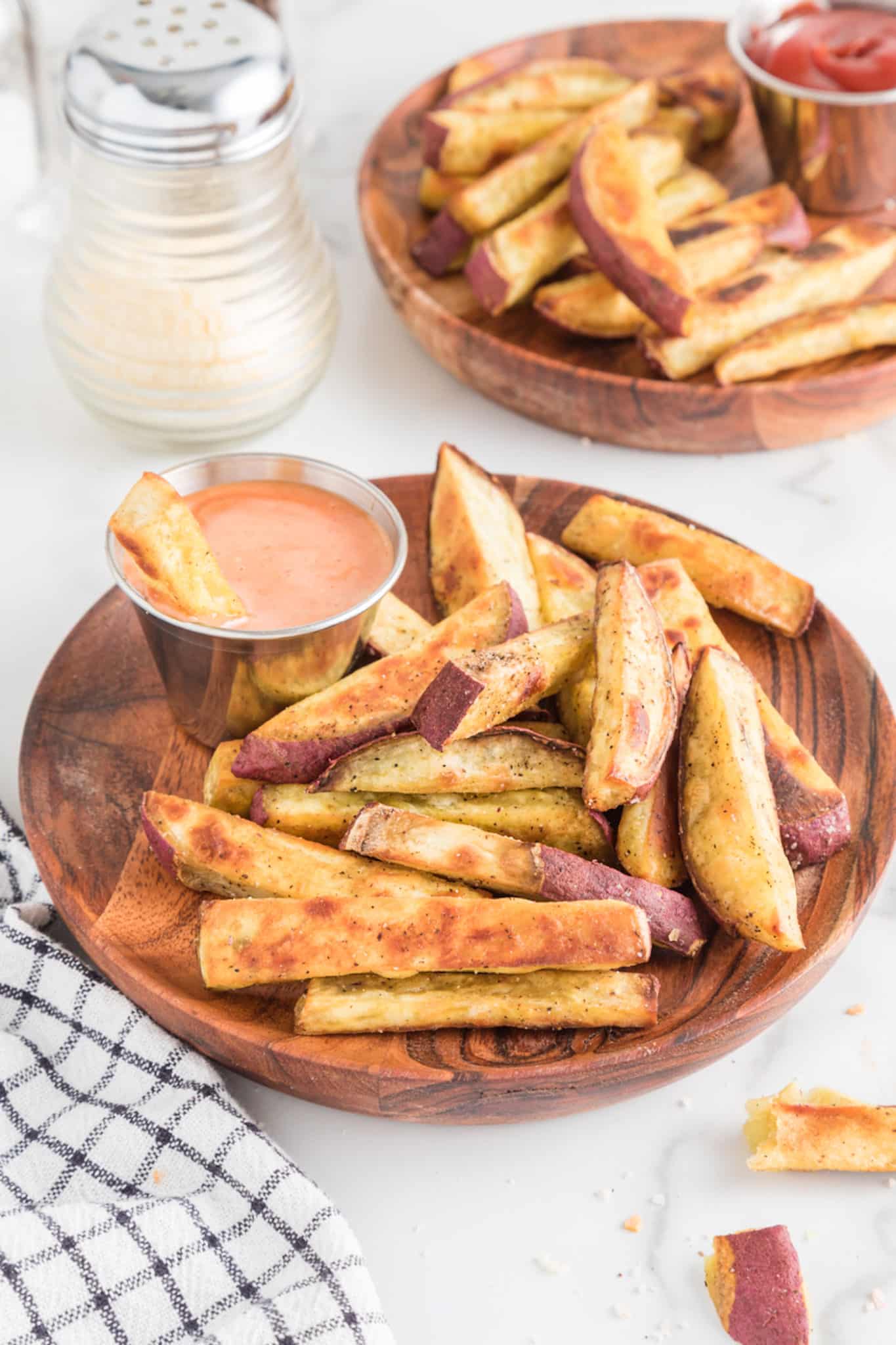 Sweet potato fries and a silver bowl of dip on a wooden plate.