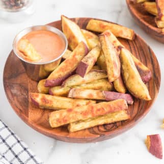 Sweet potato fries and a silver bowl of dip on a wooden plate.
