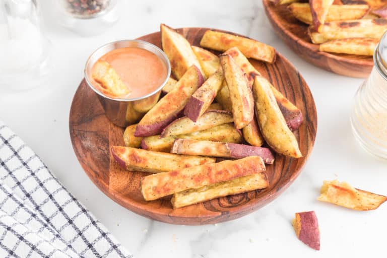 Sweet potato fries and a silver bowl of dip on a wooden plate.