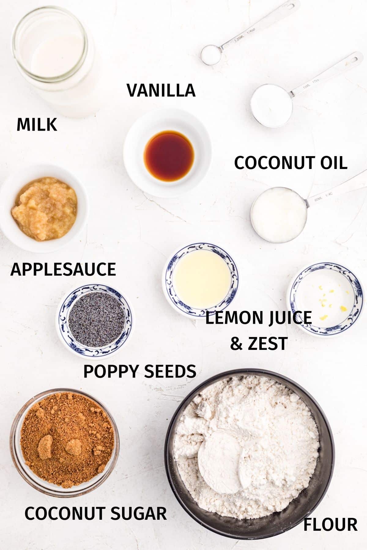 Ingredients for gluten-free vegan lemon poppy seed muffins in small bowls on a white surface.