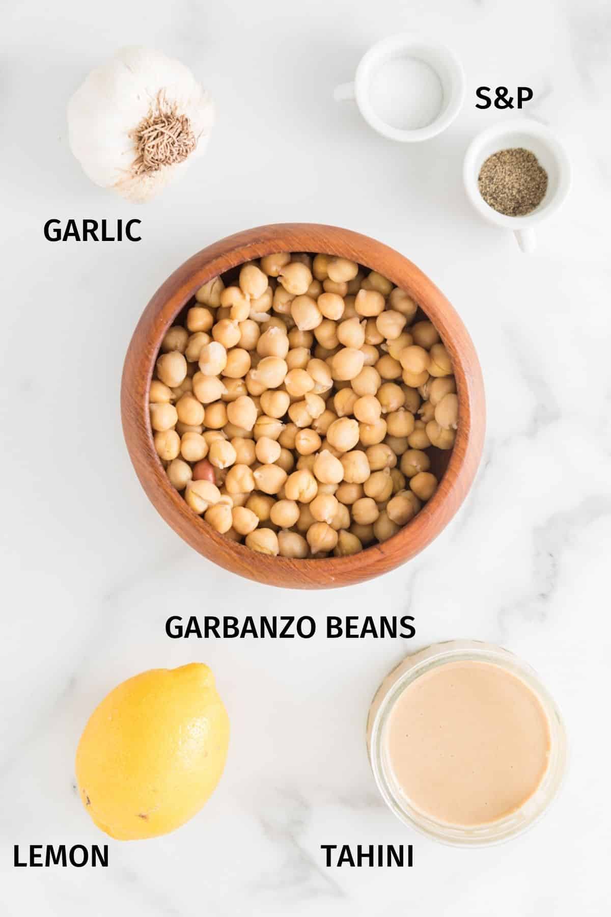 Ingredients to make oil-free hummus in small bowls on a white surface.