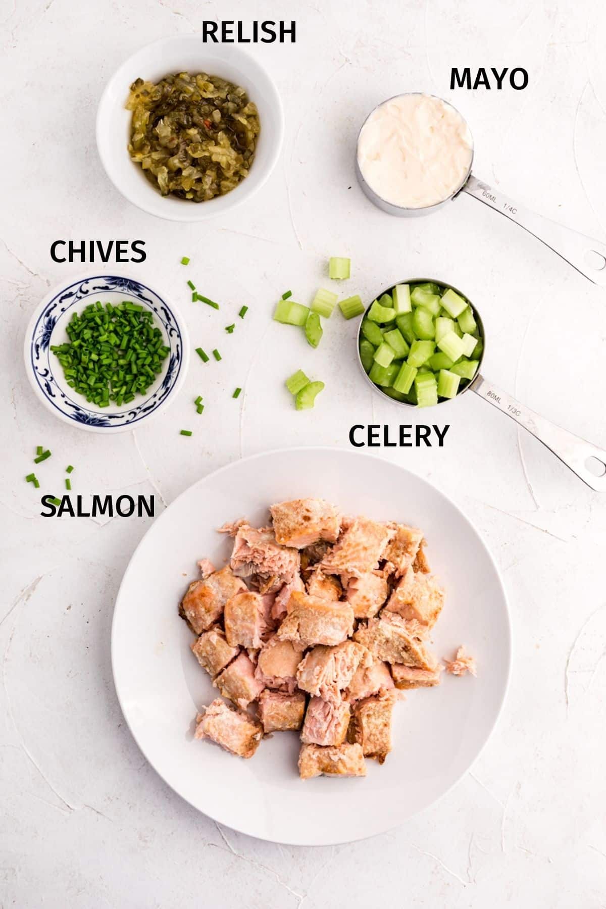 Salmon salad ingredients in small bowls on a white surface.