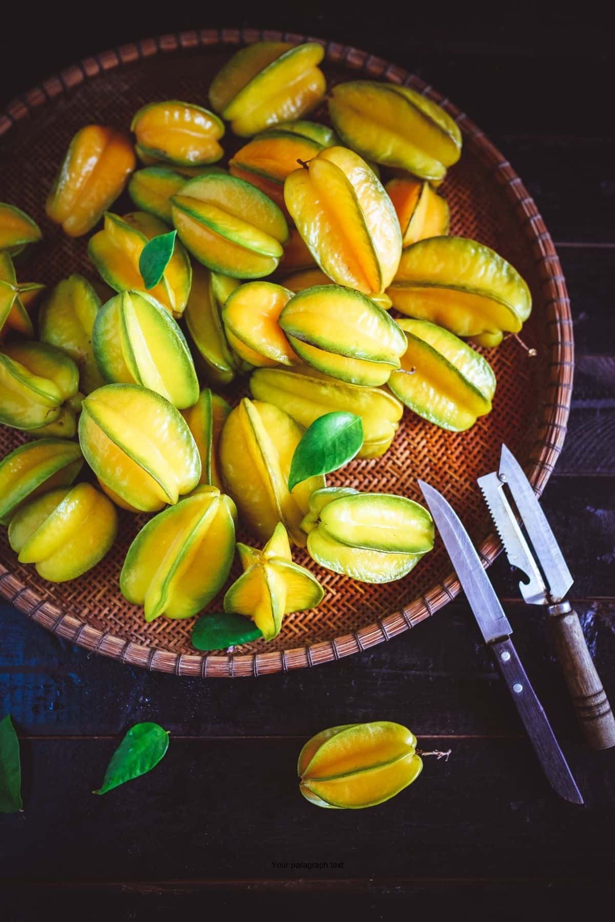 Starfruit in a wood basket with knives next to it.