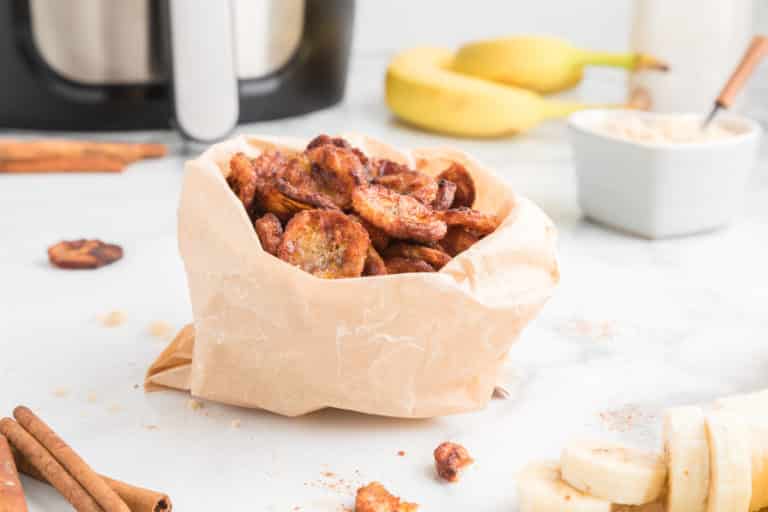 A wide angle shot of a small paper bag filled with cinnamon banana chips.