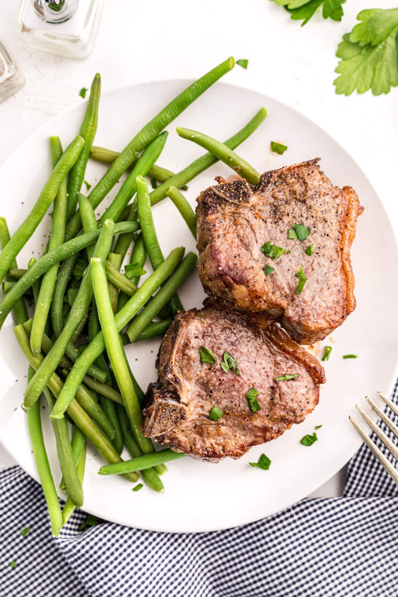 Cooked lamb chops on a white platter with cooked green beans.