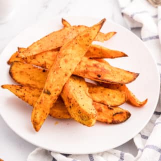 Air fryer sweet potato wedges piled up on a white plate.