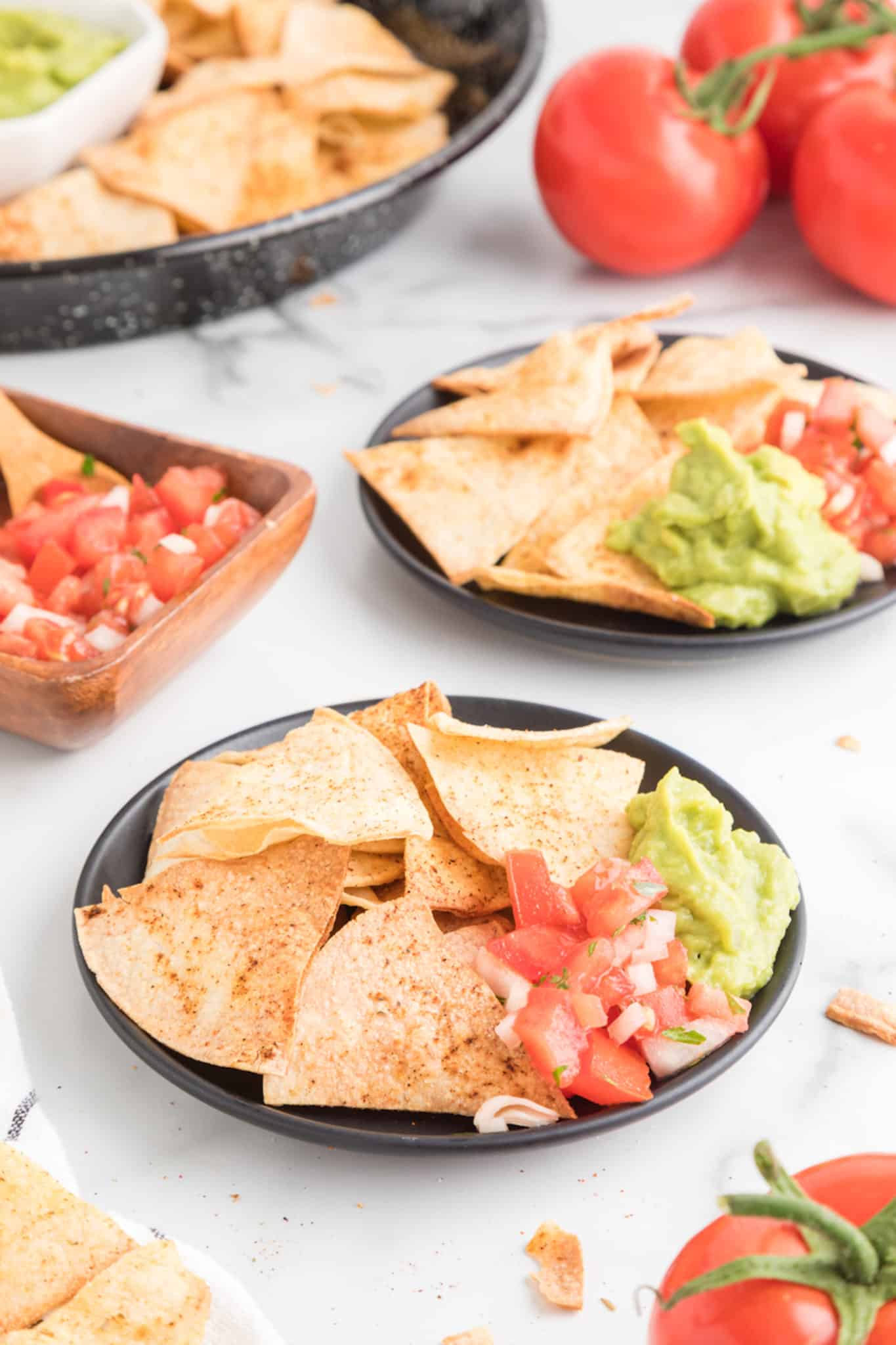 Two small black plates of fresh tortilla chips with salsa and guacamole.