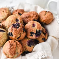 Blueberry mini muffins in a towel-lined basket next to a mug of coffee.