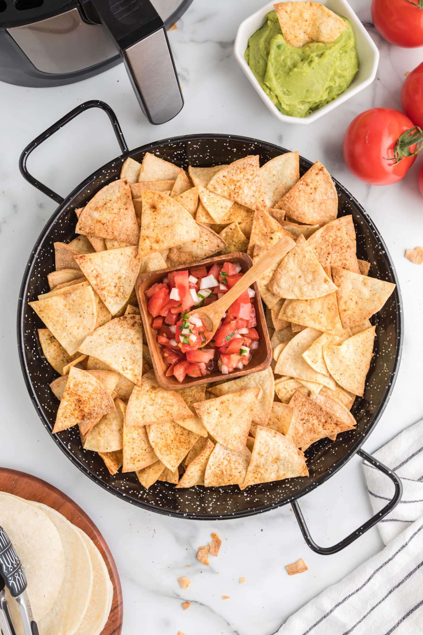 Top view of a large black platter of fresh tortilla chips surrounding a bowl of salsa.
