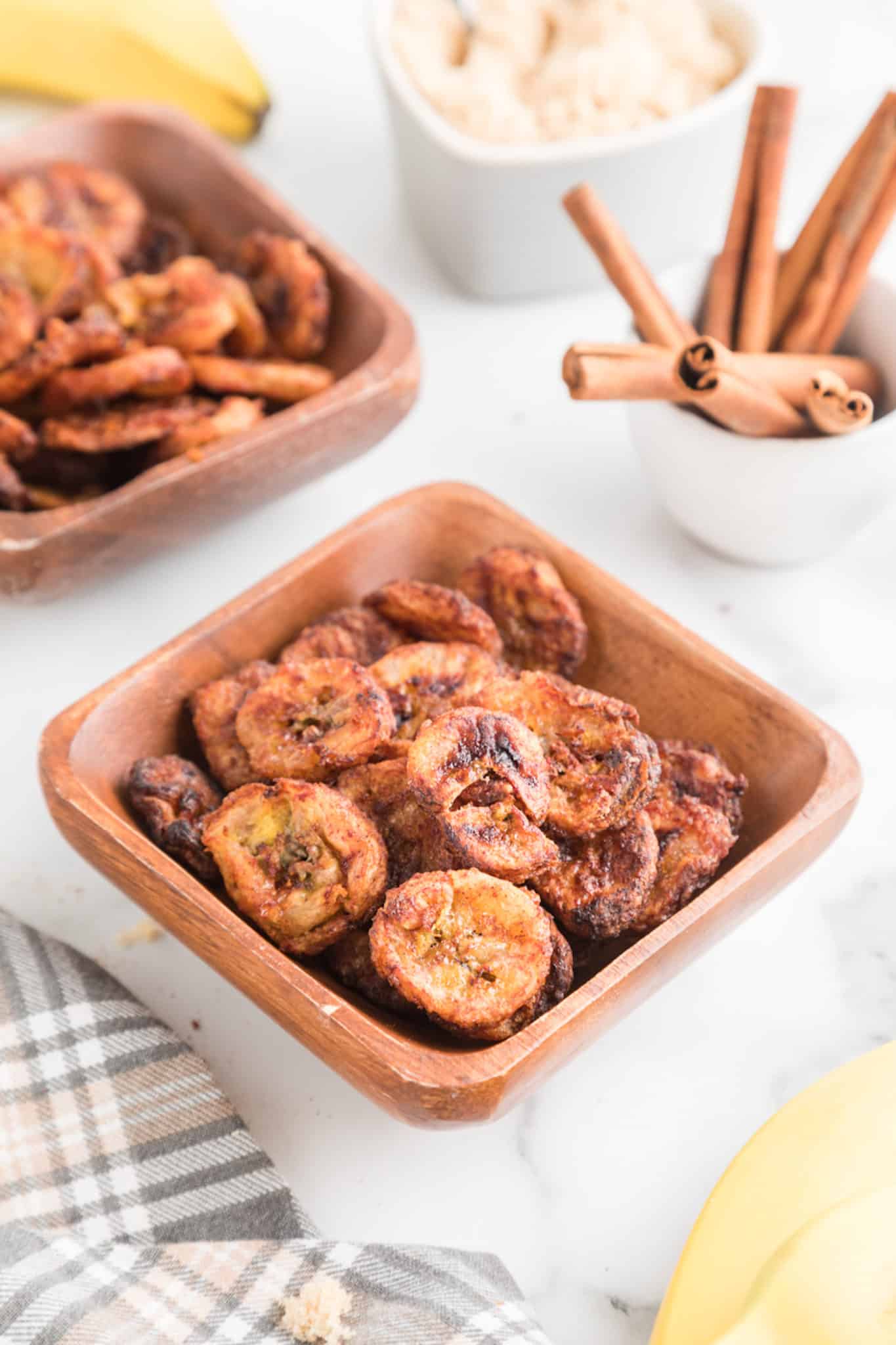 A square wooden bowl filled with air fryer cinnamon banana chips.