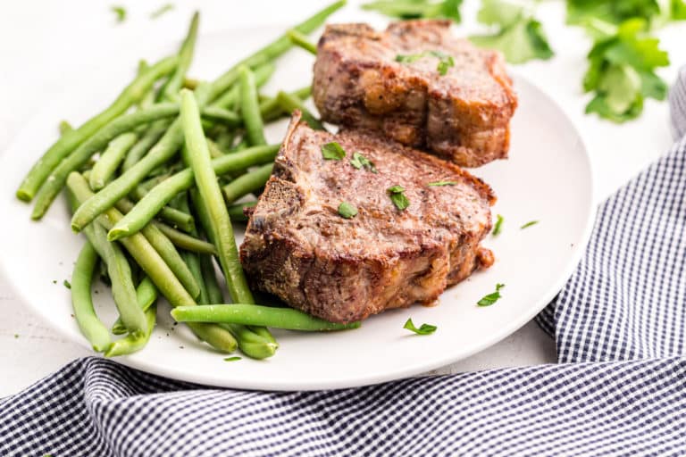 Cooked lamb chops on a white platter with cooked green beans.