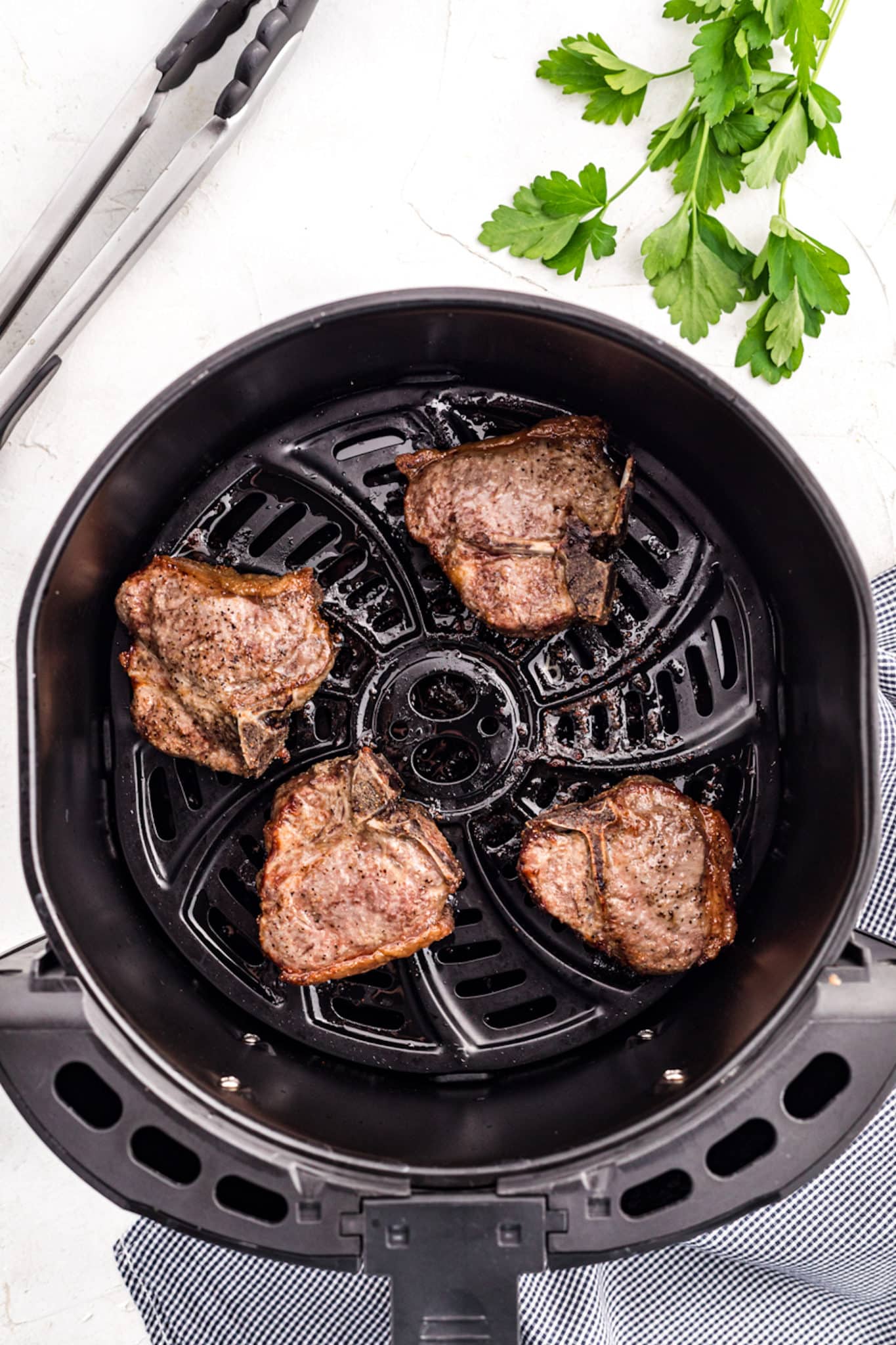 Cooked lamb chops in the basket of an air fryer.
