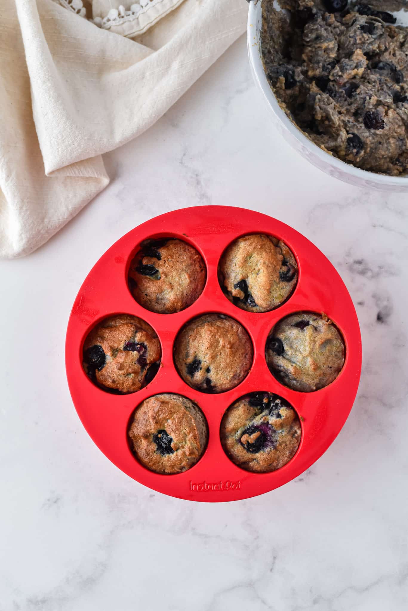 A red silicone muffin mold with 6 baked blueberry muffins.
