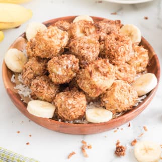 Air fryer banana fritters in a wooden bowl on a white counter.