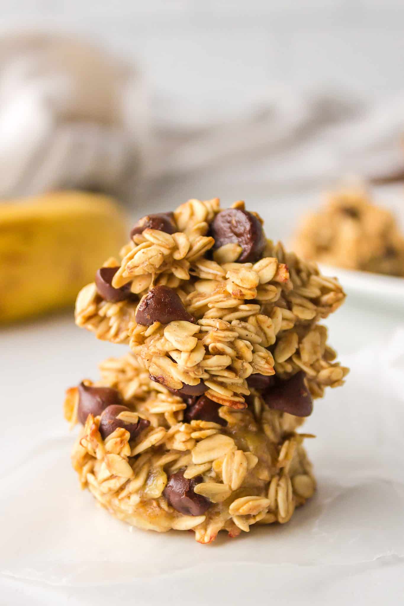 Two banana oatmeal cookies stacked on a white surface.