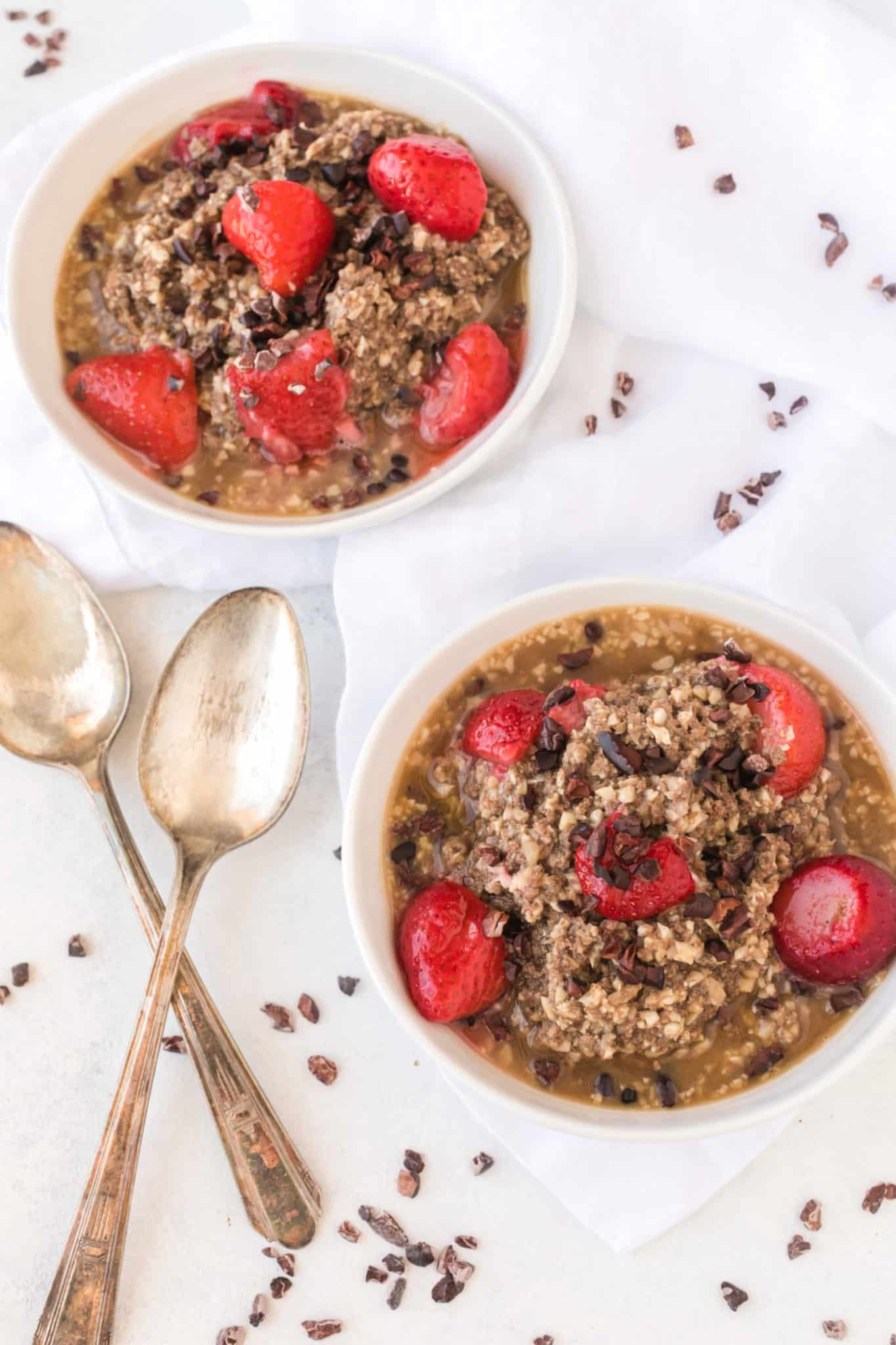 two bowls of cauliflower oatmeal with cacao nibs and strawberries.