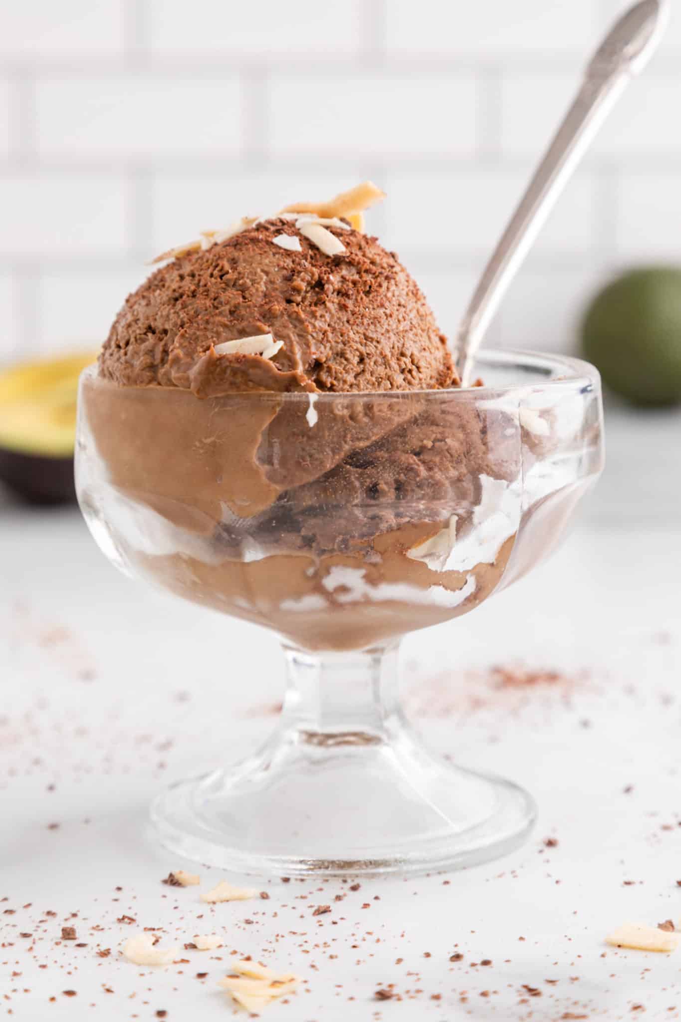 Side view of a glass parfait dish holding a spoon and two scoops of chocolate avocado ice cream.