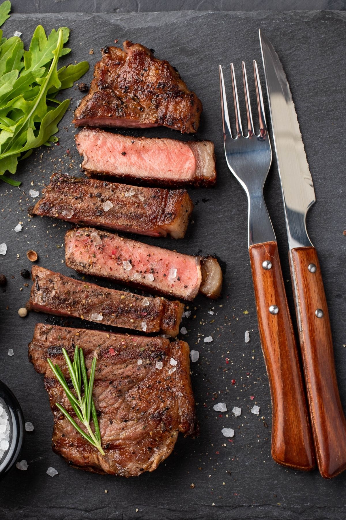cooked bison steak on slate slab with fork and knife.