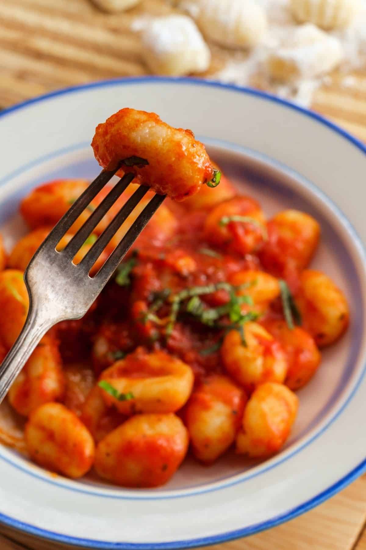 fork with cooked vegan gnocchi covered with red sauce.