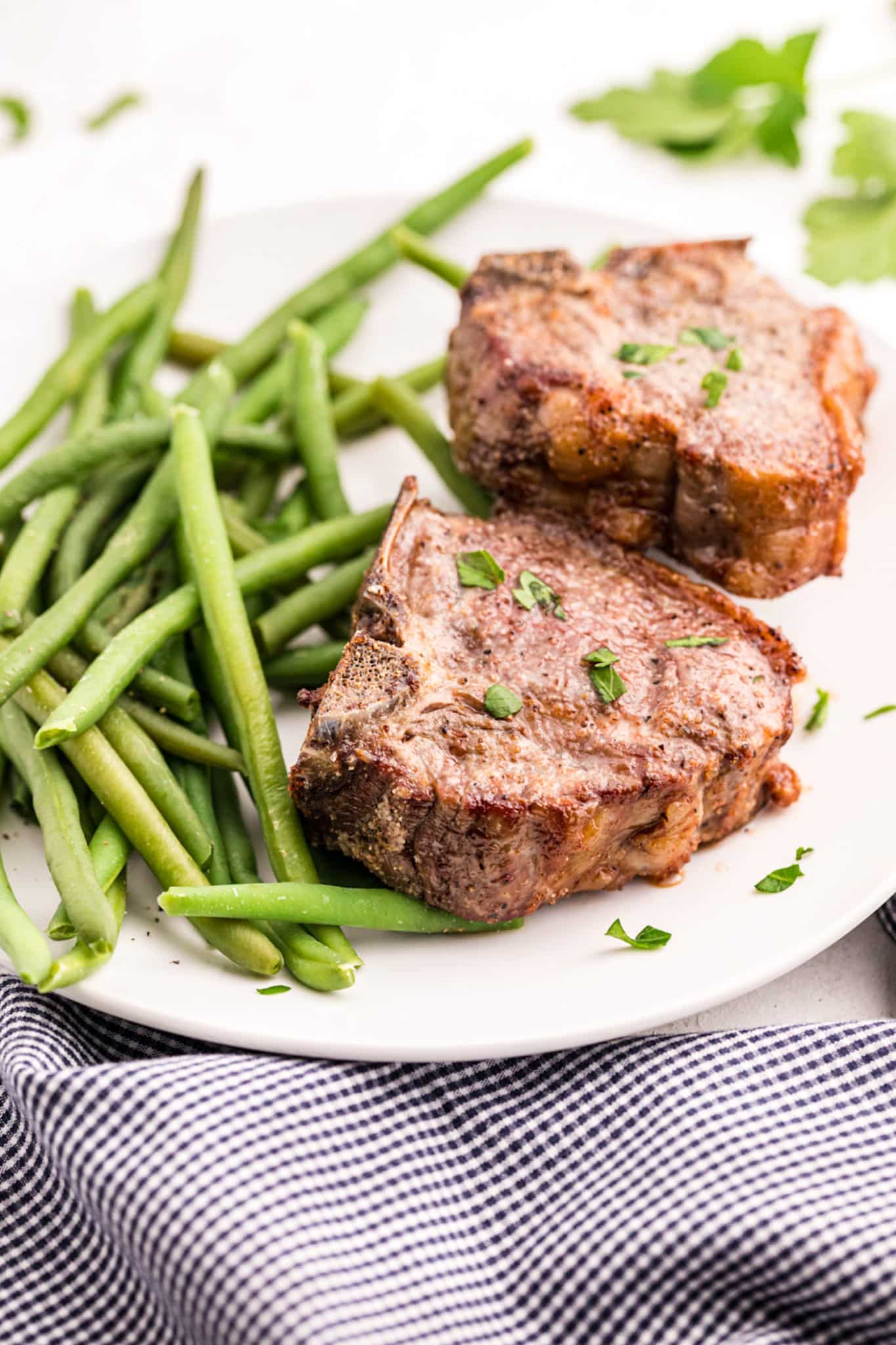 Cooked lamb chops on a white platter with cooked green beans.