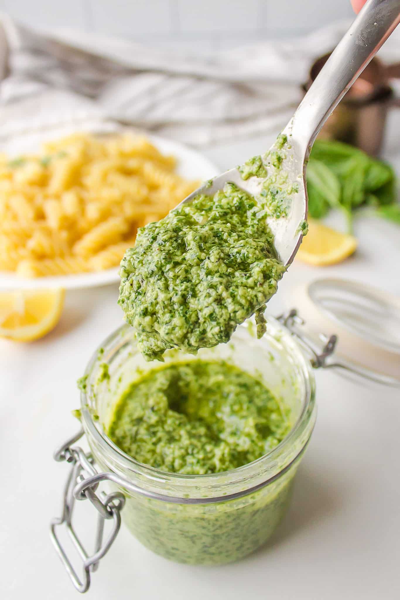 A spoon holding up a scoop of dairy free pesto from a glass jar.