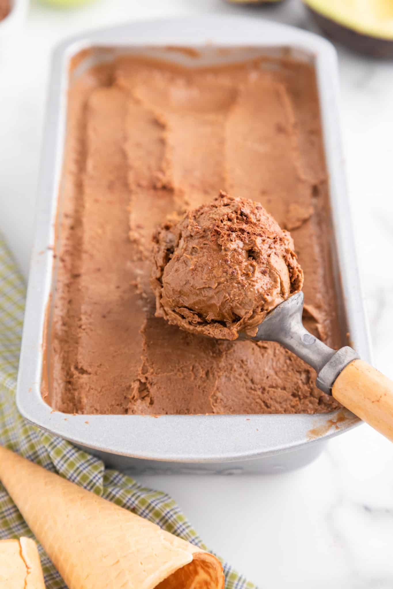 An ice cream scoop filled with chocolate avocado ice cream from a metal loaf pan.