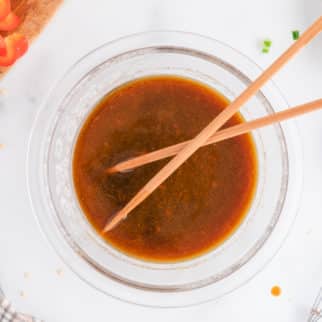 Top view of a pair of chopsticks in a small glass bowl of stir fry sauce.