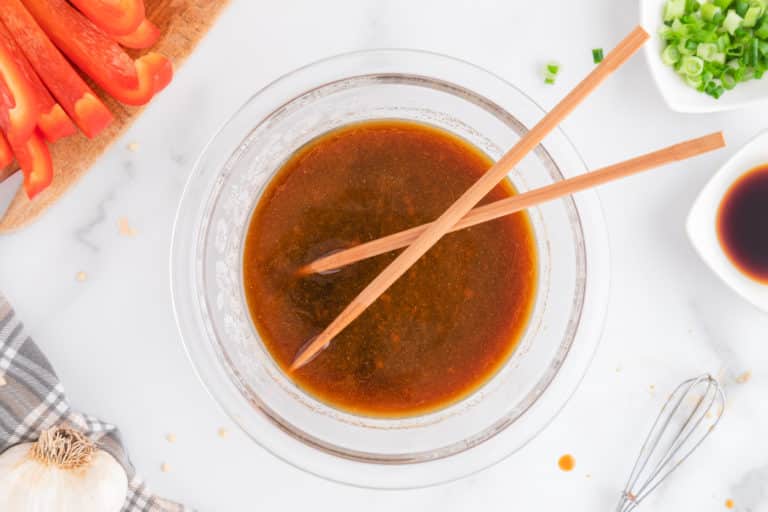 Top view of a pair of chopsticks in a small glass bowl of stir fry sauce.