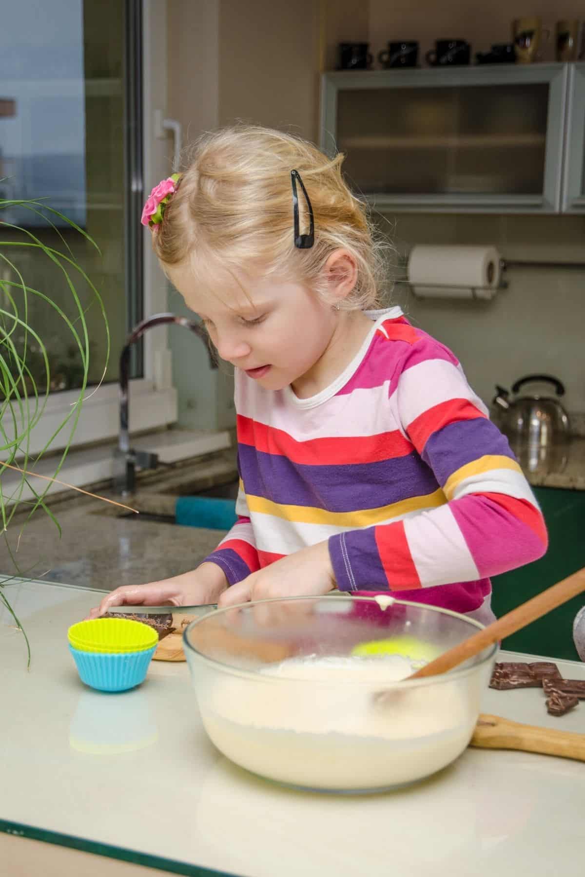 little girl making muffins in a kitchen.