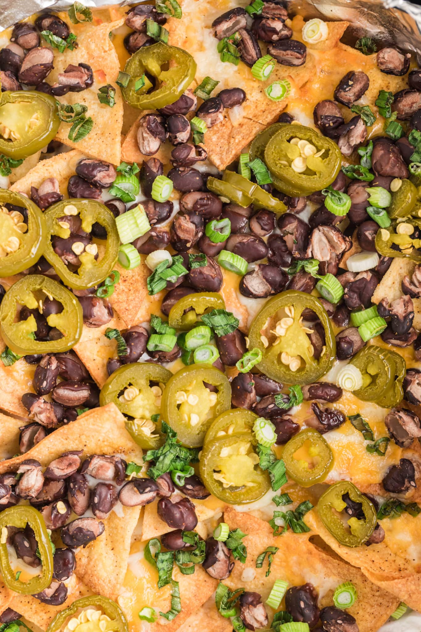 Close up view of black beans, pickled jalapenos, and cheese on tortilla chips.
