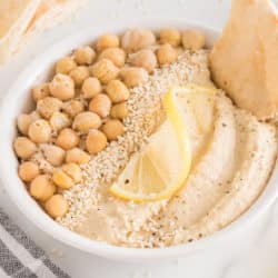 A white bowl of oil-free hummus topped with chickpeas and sesame seeds.