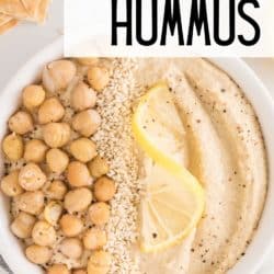 A white bowl of hummus topped with chickpeas and sesame seeds.