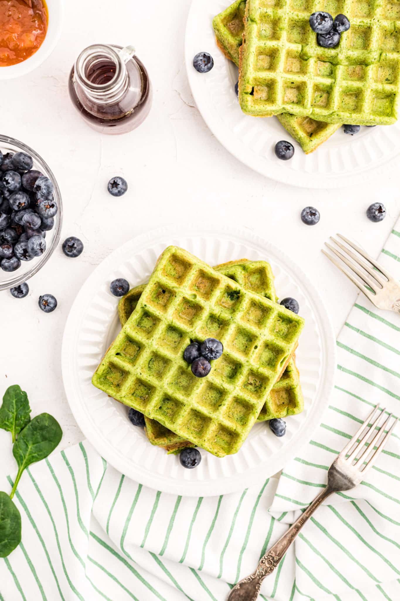 two plates of green waffles with fresh blueberries and syrup.