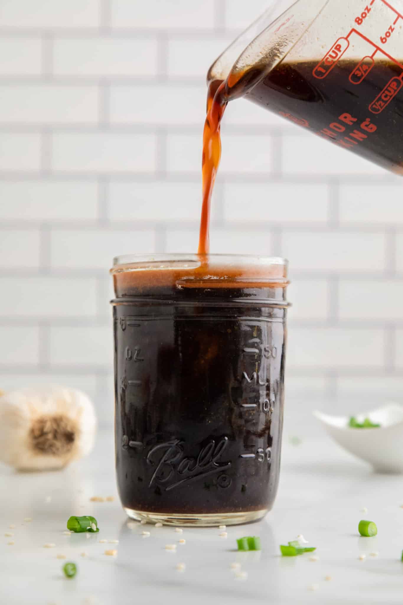 A glass measuring cup pouring stir fry sauce into a mason jar.