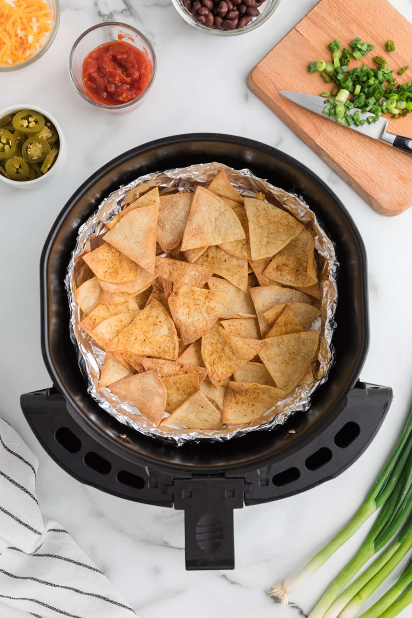 Top view of an air fryer basket lined with foil and filled with homemade tortilla chips.
