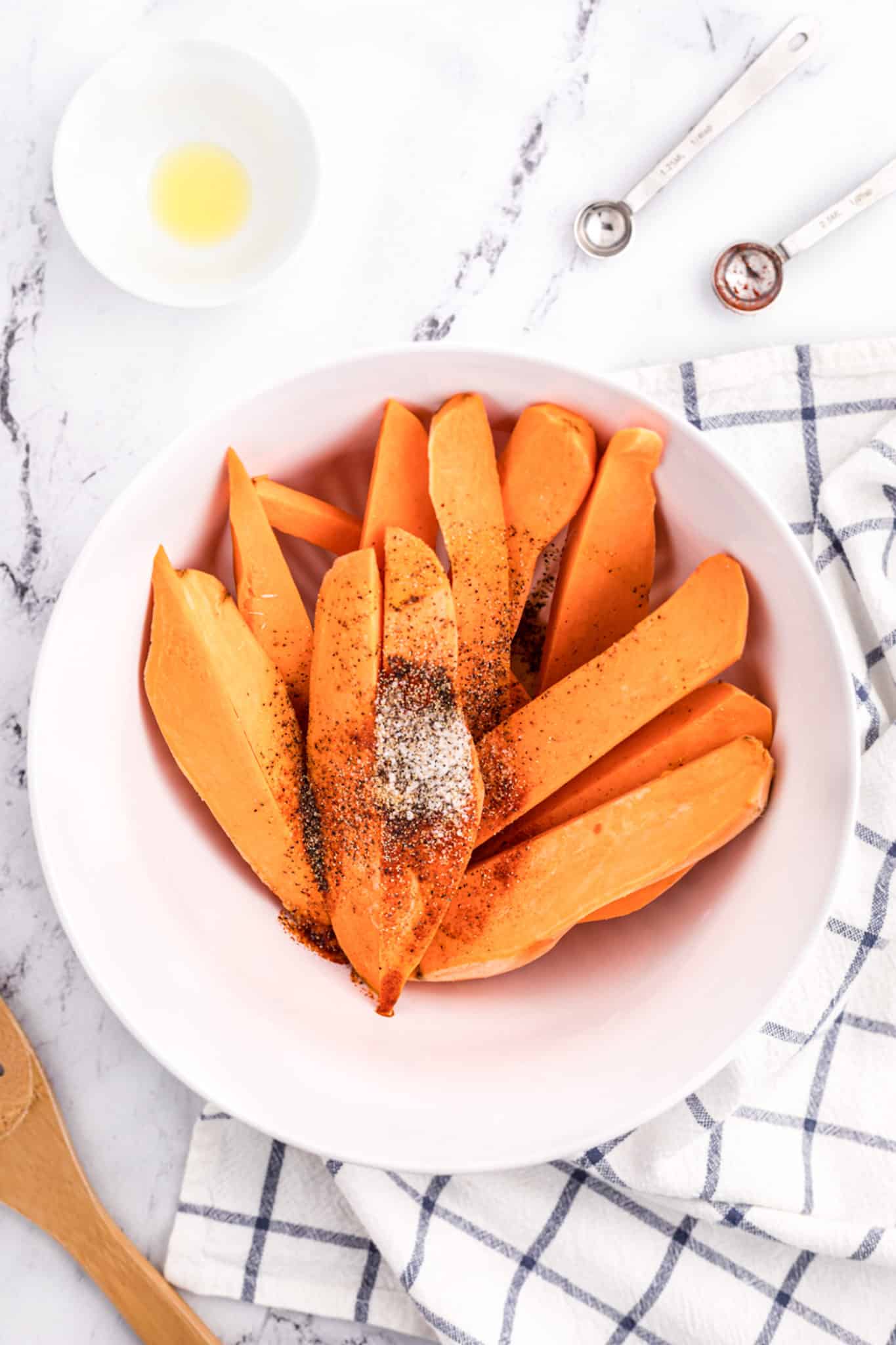 Sweet potato wedges in a white bowl with spices on top.
