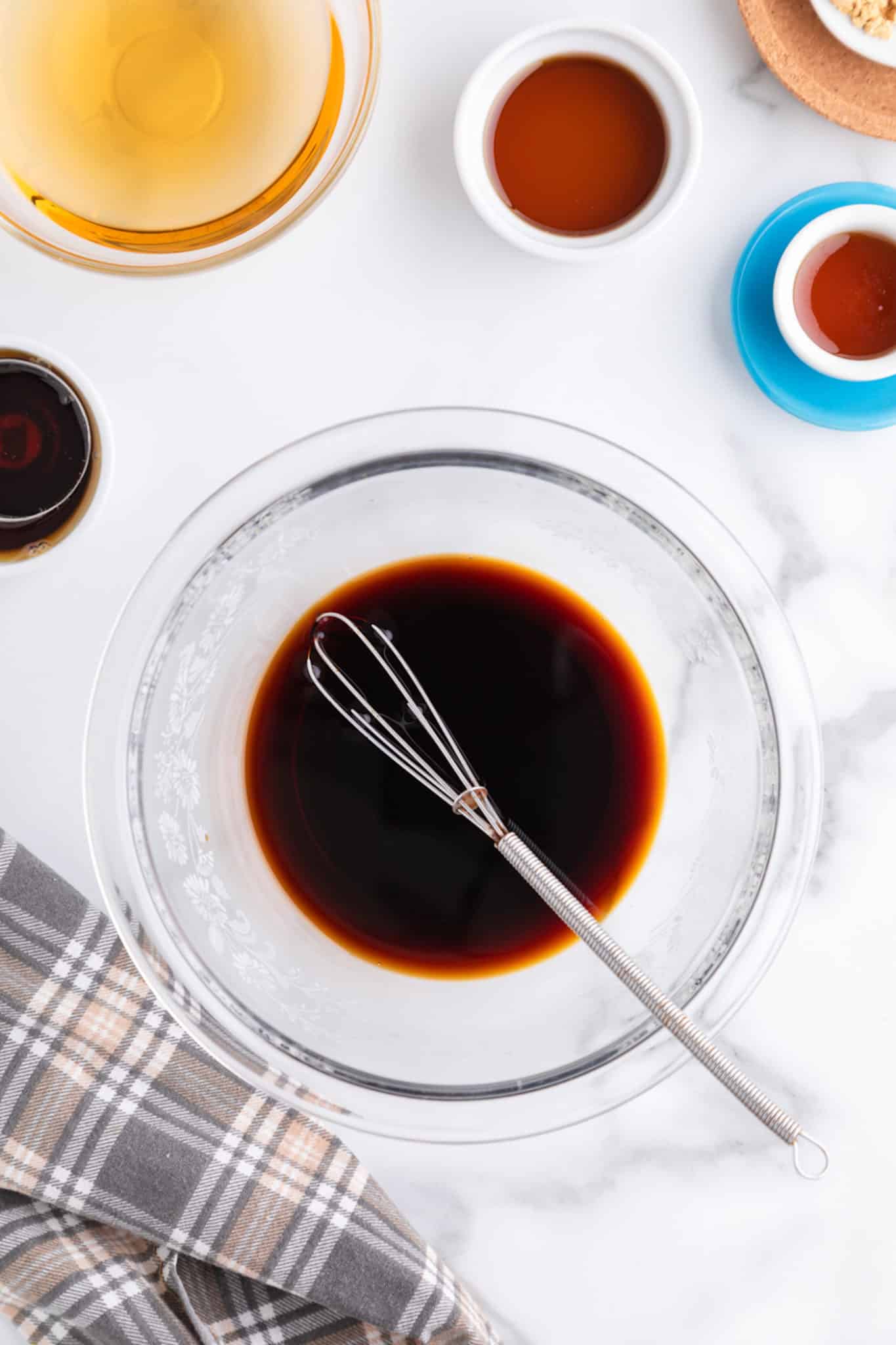 A small silver whisk in a glass bowl of soy sauce.