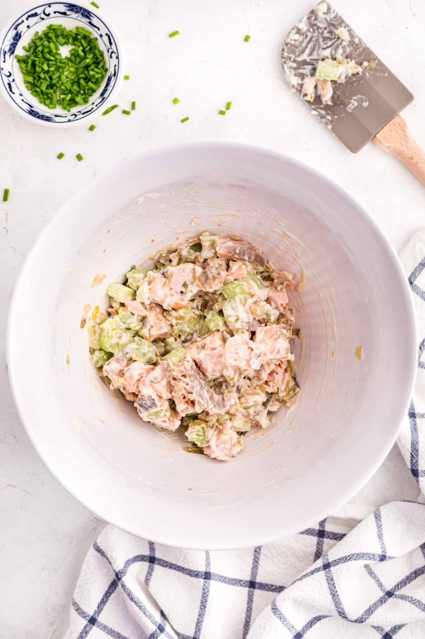 Salmon salad mixed up with mayo in a large white mixing bowl.