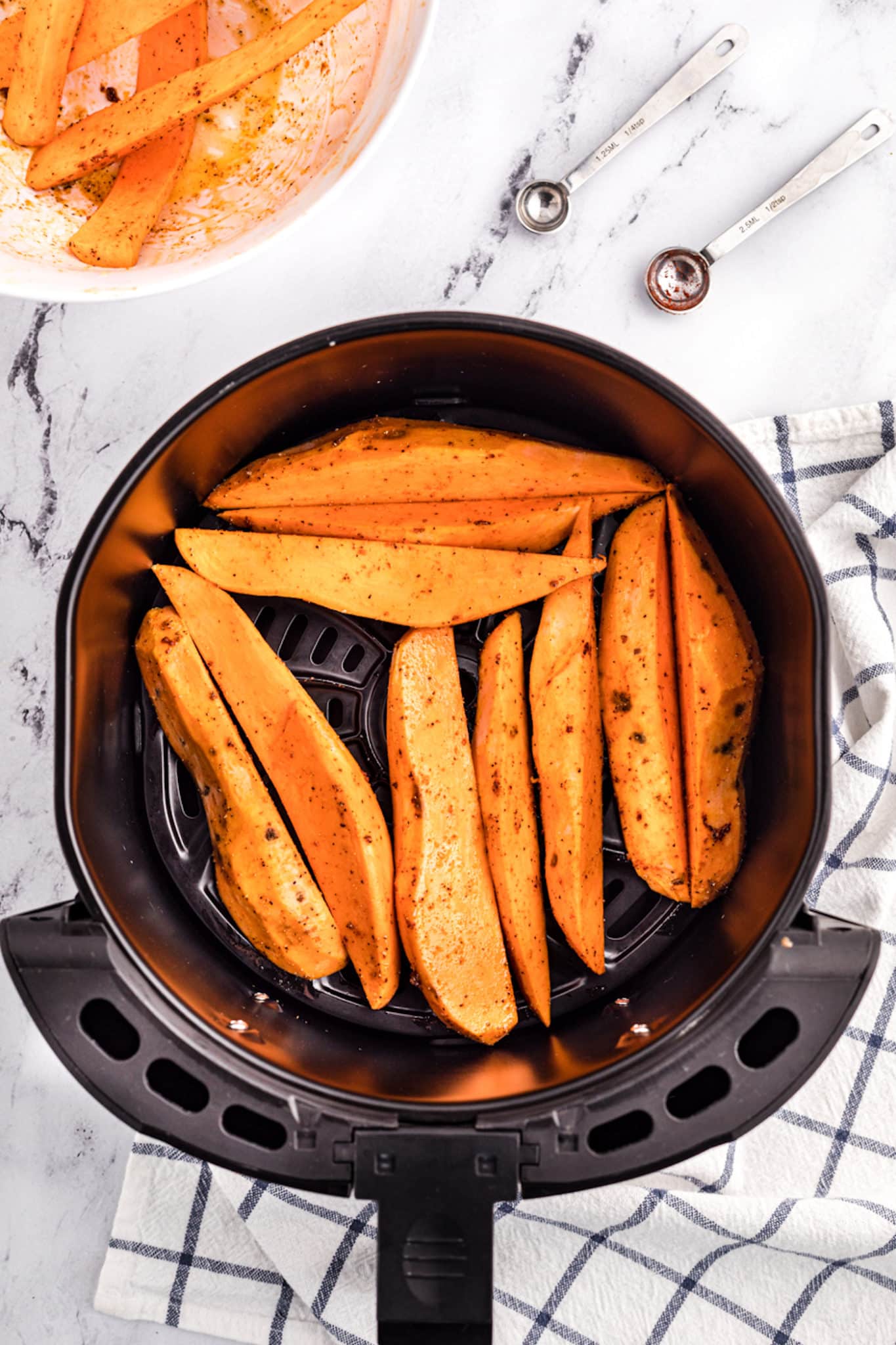 Sweet potato wedges in the basket of an air fryer.