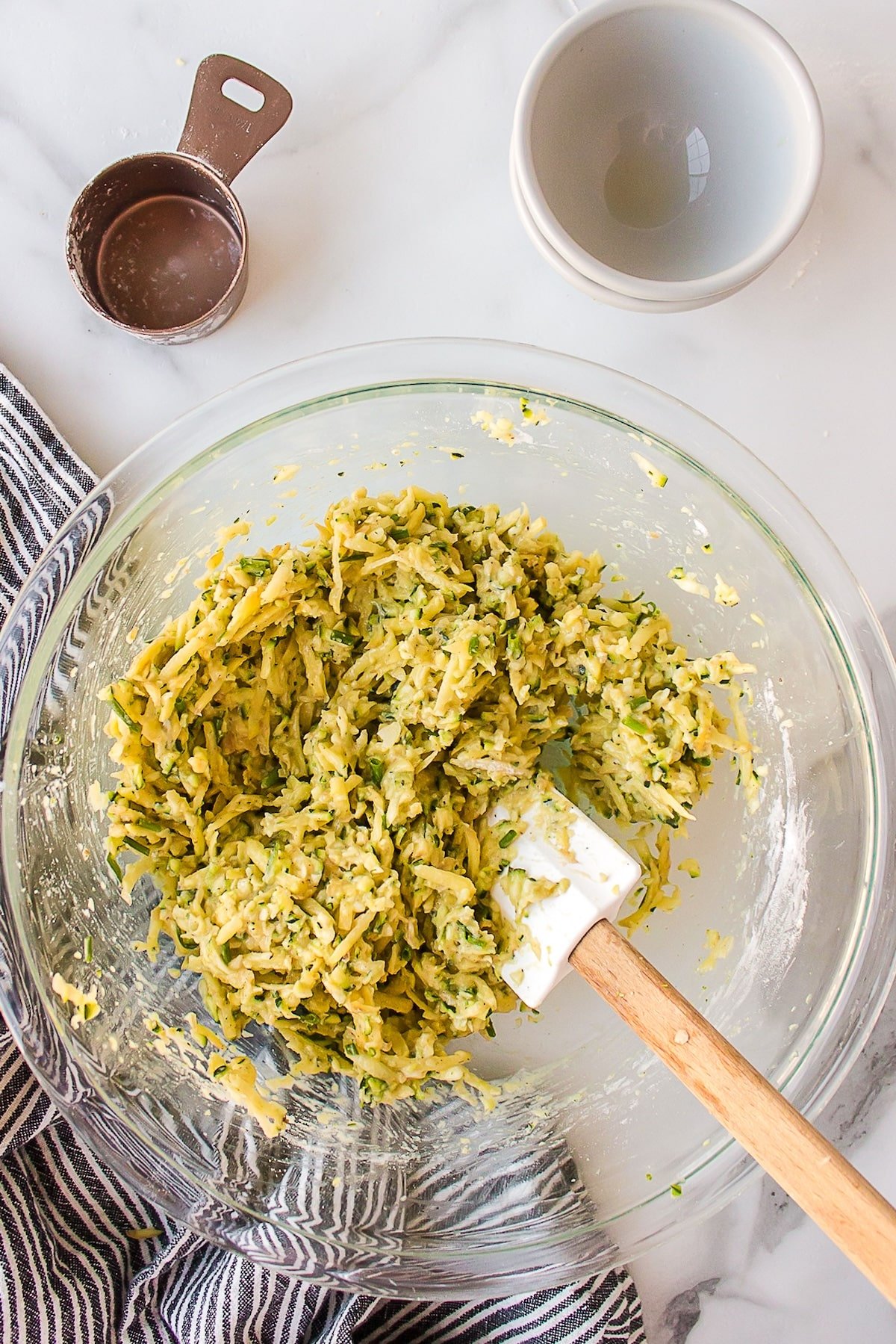 making zucchini potato fritters in bowl with spatula.