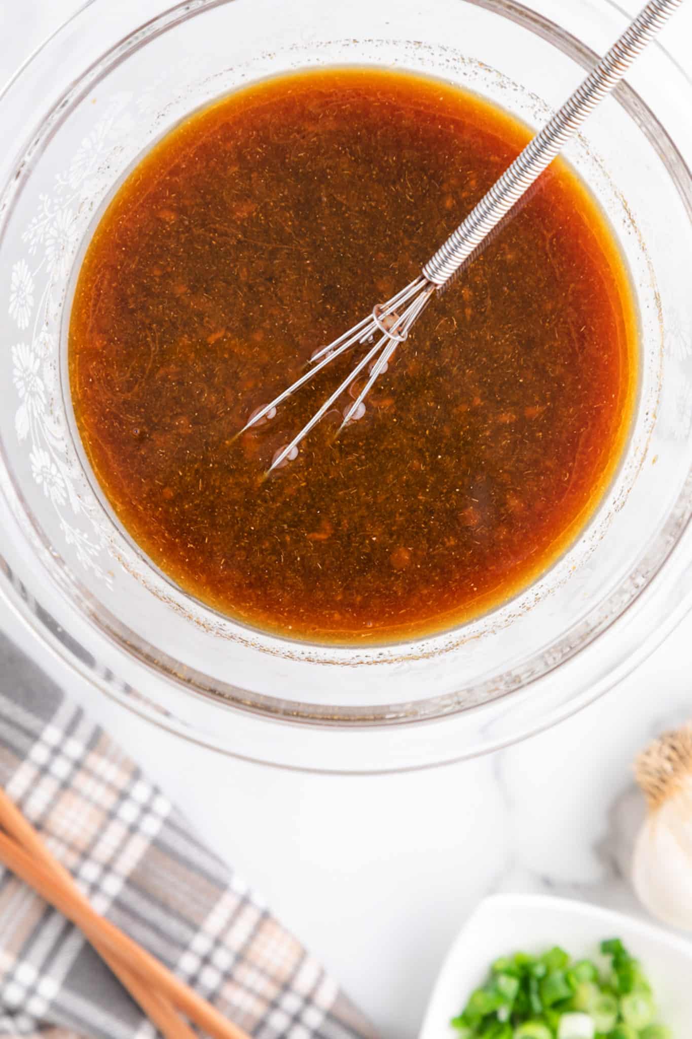 A whisk in a clear glass bowl of stir fry sauce.