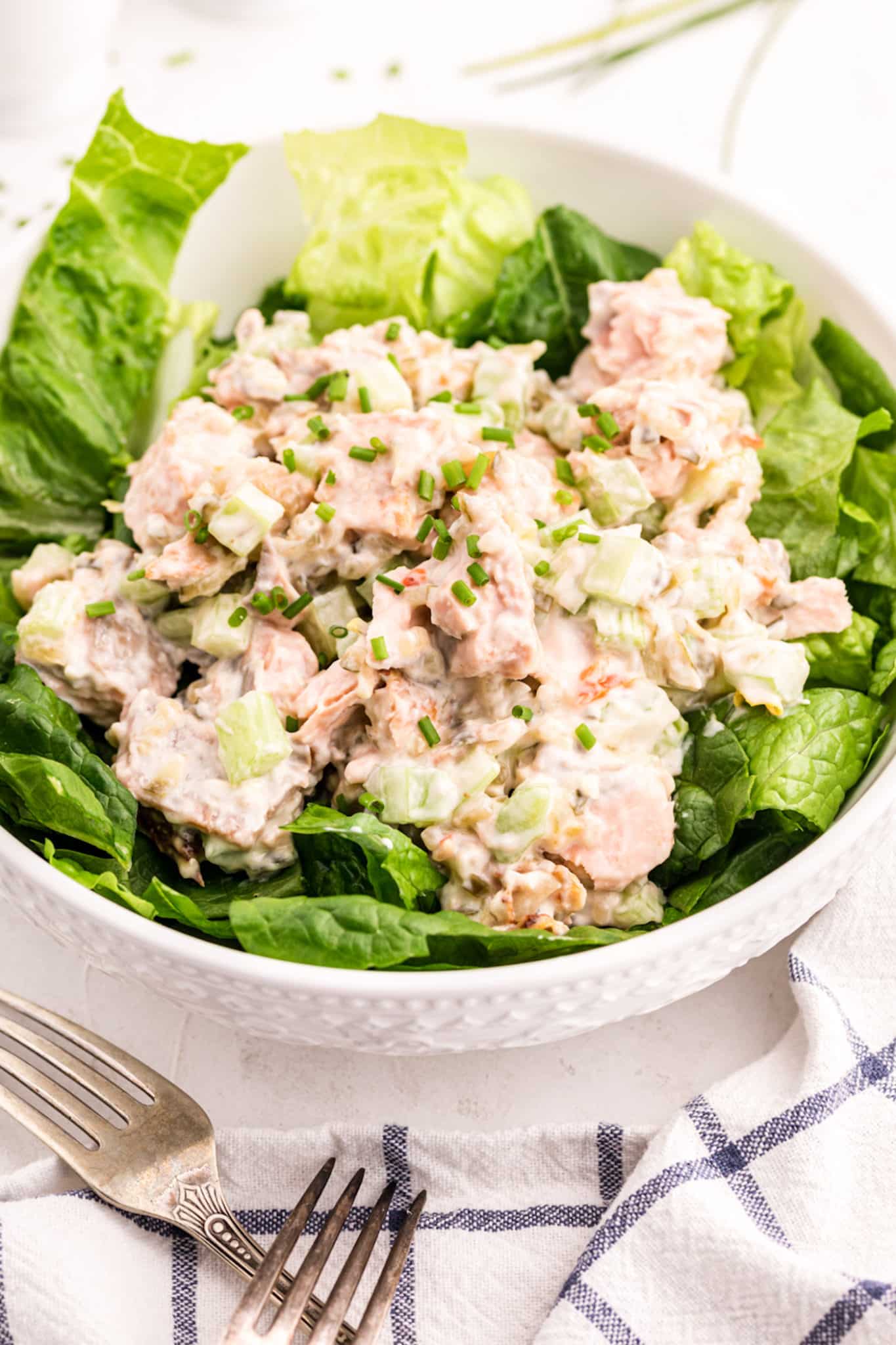 Salmon salad with celery and mayo topping lettuce in a large white bowl.