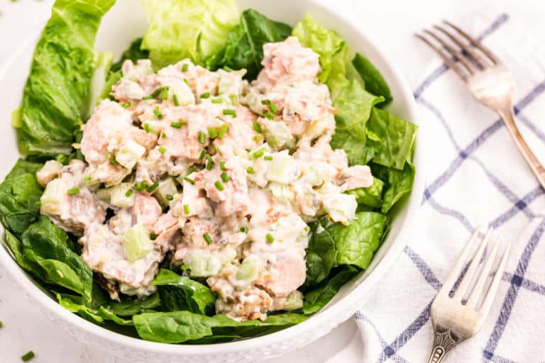 Two forks on a checkered napkin next to a white bowl of lettuce and salmon salad.