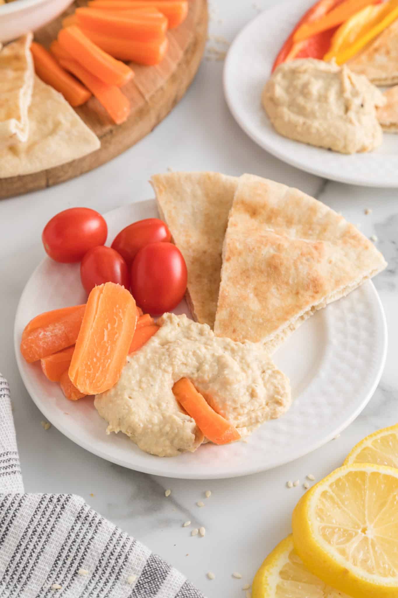 Oil free hummus with veggies and pita on a small white plate.